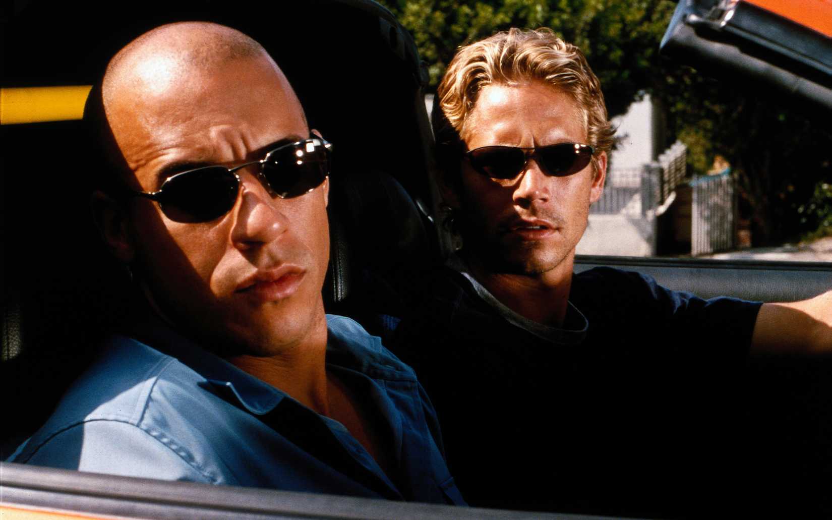 Vin Diesel and Paul Walker wear sunglasses with furrowed brows in a convertible in The Fast and The Furious