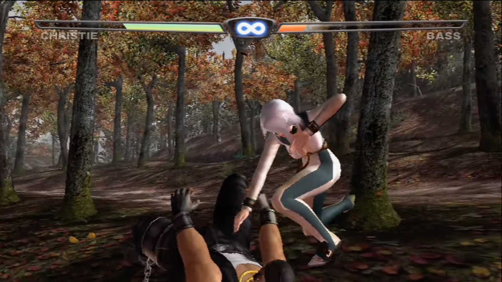 An in-game screenshot of Dead or Alive 3, with Christie pinning Bass down in the forest.